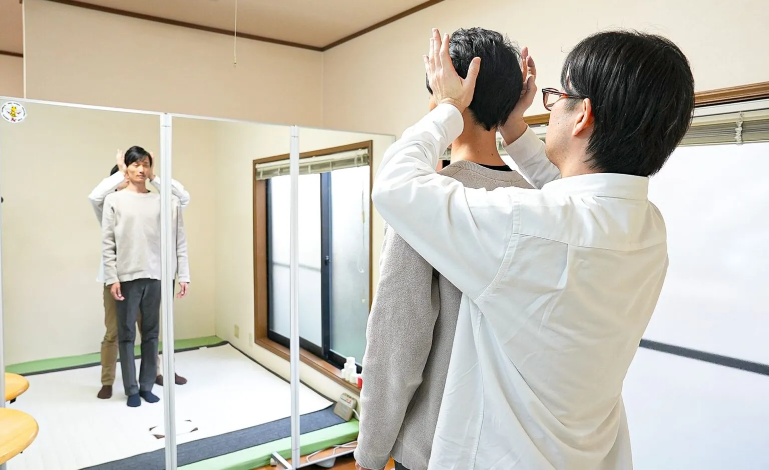 大きな鏡の前で、院長が姿勢を指し示しながら来院者へ説明している様子